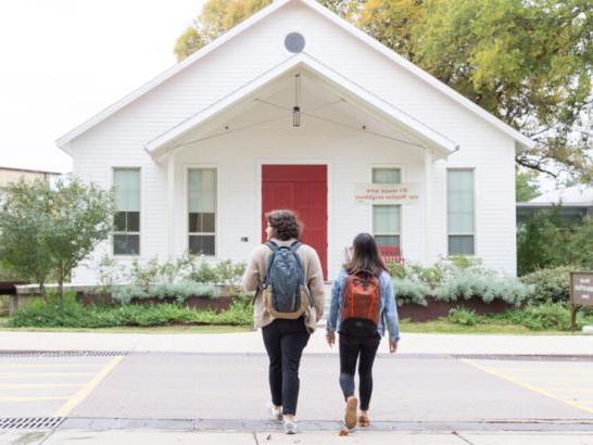 Two students wearing backpacks walk towards the front of Our Lady Queen of Peace Chapel.